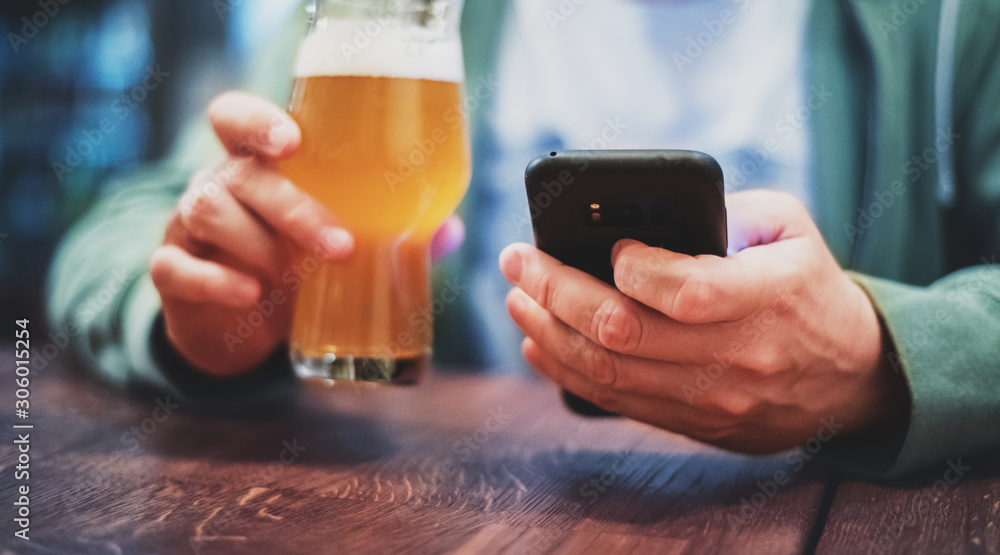 close up of man hand hold smartphone, drinking beer and reading message at bar or pub