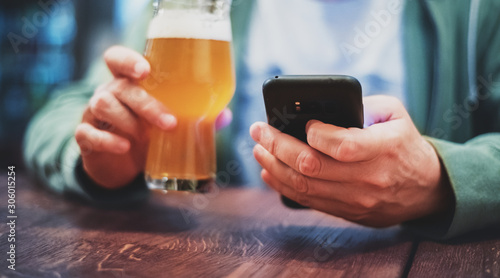Obraz na plátně close up of man hand hold smartphone, drinking beer and reading message at bar o
