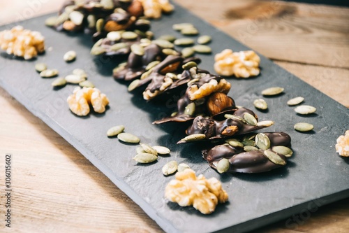 healthy snack made of almonds, walnuts, hazelnuts and pumpkin seeds covered in dark chocolate standing on a slate dish on a wooden base and black background