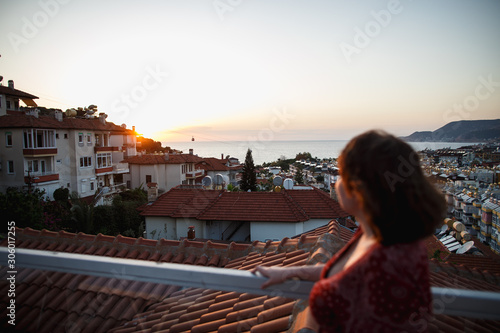 Fototapeta Naklejka Na Ścianę i Meble -  Summer outdoor portrait of young pretty sensual girl posing at roof at sunset. Fluing hair on wind. View on mediterranian city buildings and red roofs.
