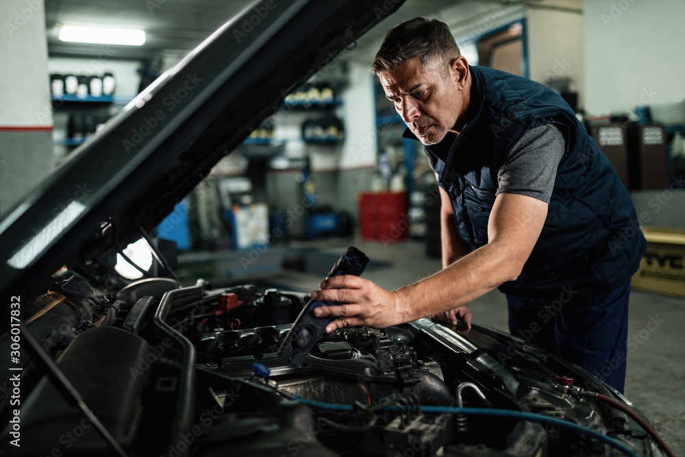 Auto mechanic checking engine under the hood at repair shop. Auto mechanic checking engine under the hood at repair shop.