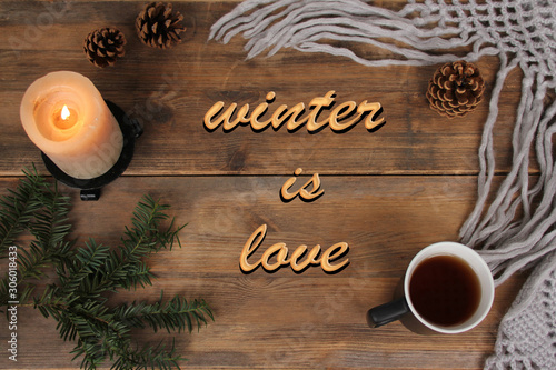 candle burns on a wooden table, mug of tea, knitted shawl, coniferous branches, concept winter mood, winter is love, copy space