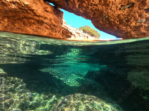 Underwater above and below photo of rocky seascape arch forming a beautiful emerald lagoon in tropical exotic island