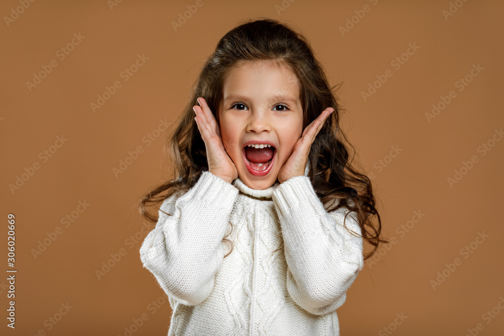happy surprised beautiful curly little child girl in white sweater looking to camera on beige background. Human emotions and facial expression happy surprised beautiful curly little child girl in white sweater looking to camera on beige background. Human emotions and facial expression