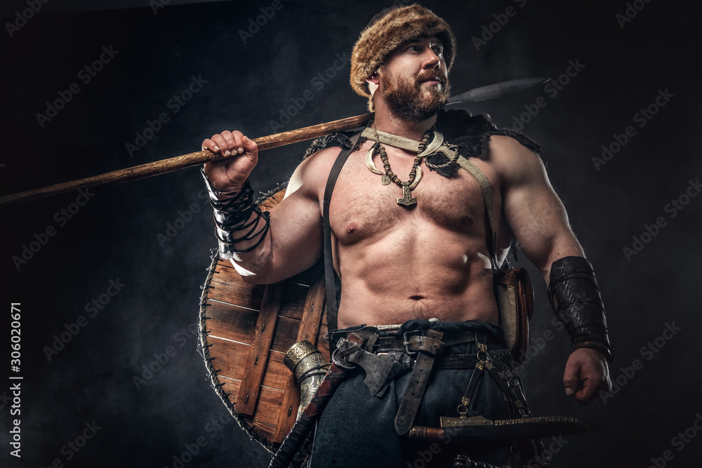 Severe barbarian in warrior clothes, posing on a dark background. Severe barbarian in warrior clothes, posing on a dark background.