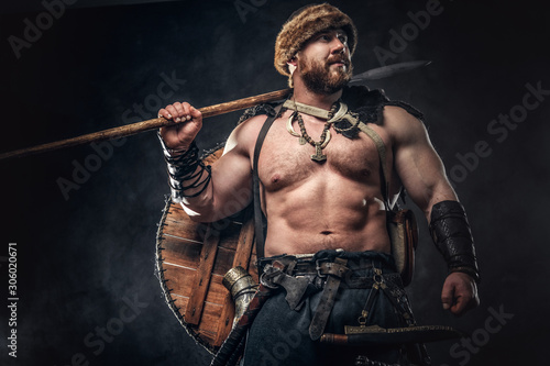 Severe barbarian in warrior clothes, posing on a dark background. © Fxquadro