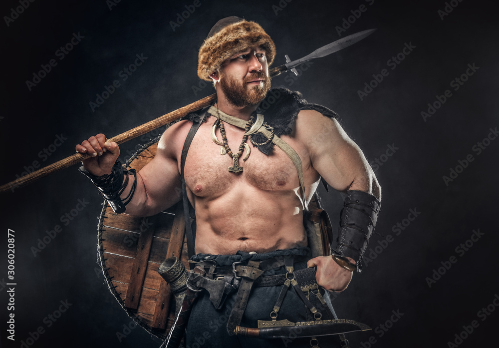 Severe barbarian in warrior clothes, posing on a dark background. Severe barbarian in warrior clothes, posing on a dark background.