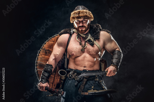 Fototapeta Naklejka Na Ścianę i Meble -  Severe barbarian in warrior clothes, posing on a dark background.