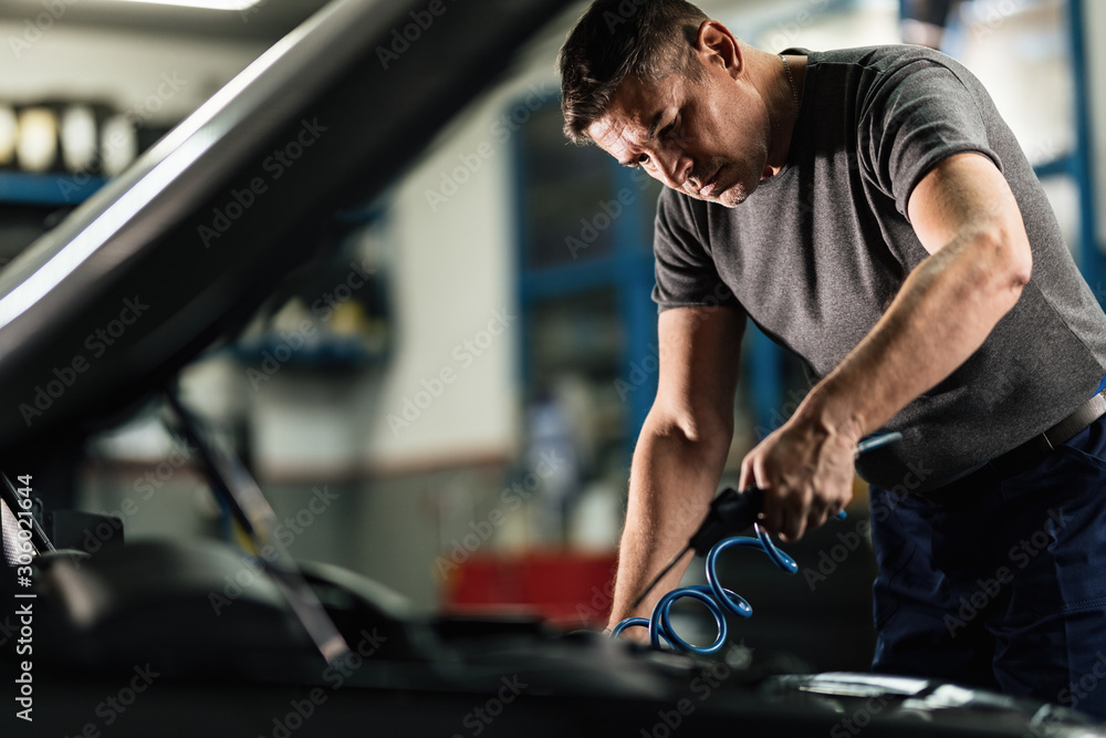 Mid adult mechanic working on car engine in auto repair shop. Mid adult mechanic working on car engine in auto repair shop.