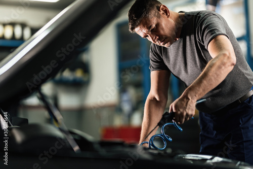 Mid adult mechanic working on car engine in auto repair shop. © Drazen