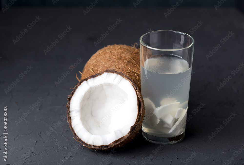 Coconut water with coconut slices, in a glass glass, a whole coconut and half a nut, dark stone background Coconut water with coconut slices, in a glass glass, a whole coconut and half a nut, dark stone background