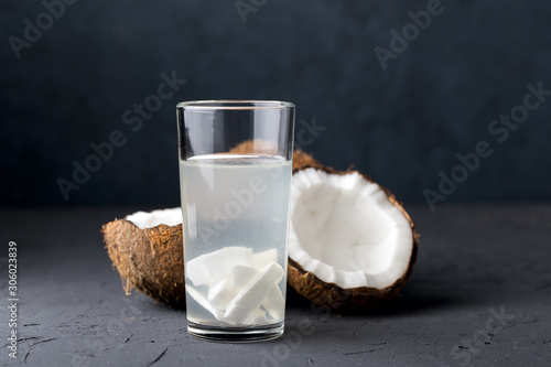 Coconut water with coconut slices, in a glass glass, a whole coconut and half a nut, dark stone background