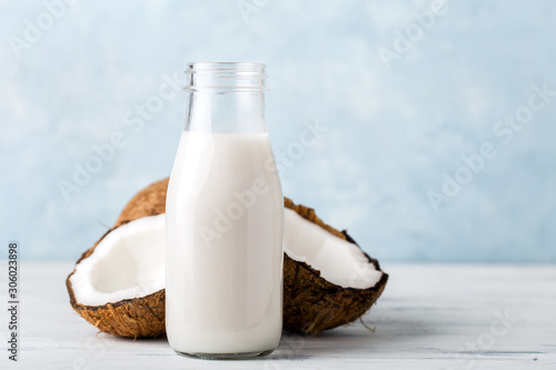 Health content, coconut milk in a glass bottle, coconut halves, light wooden table, close-up,