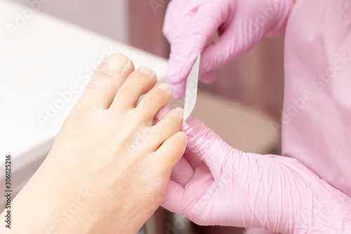 Young woman getting professional pedicure in a beauty salon  closeup. Hands a pedicurist in protective rubber gloves are applied with nails to the nails using a nail file. Professional beauty salon. 