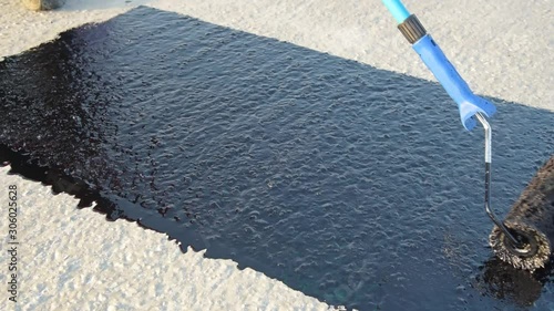 Waterproofing coating. Worker applies bitumen mastic on the foundation. Roofer cover the rooftop polymer modified bitumen waterproofing primer, with a roller brush.