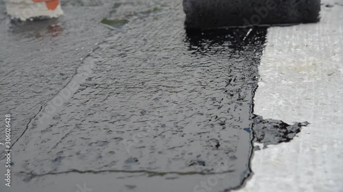 Waterproofing coating. Worker applies bitumen mastic on the foundation. Roofer cover the rooftop polymer modified bitumen waterproofing primer, with a roller brush.