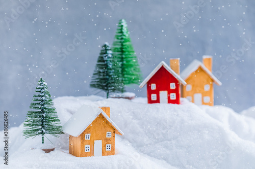 Miniature wooden houses on the snow over blurred Christmas decoration background, toned, daylight
