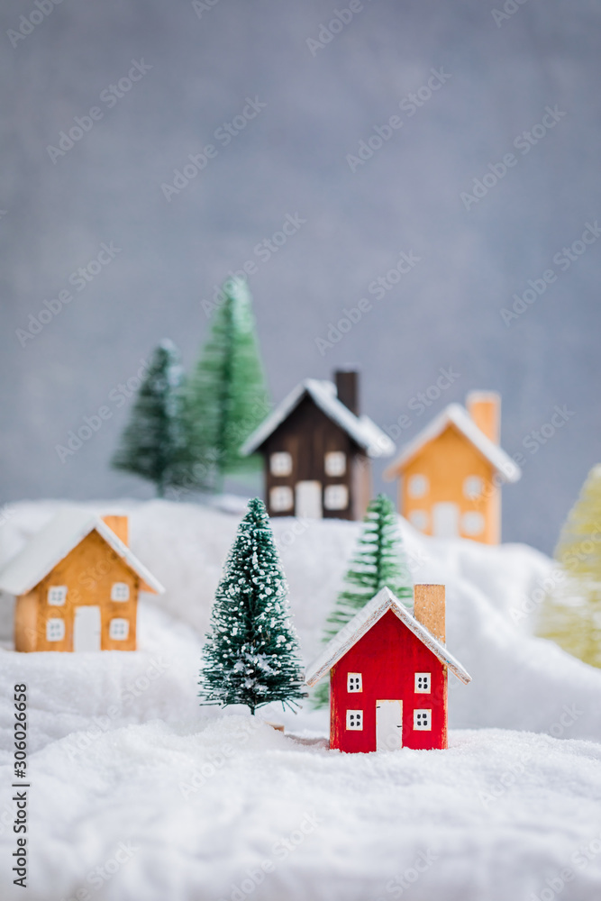 Miniature wooden houses on the snow over blurred Christmas decoration background, toned, daylight