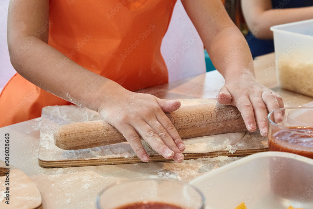 The kid 's learning to make pizza from the dough.