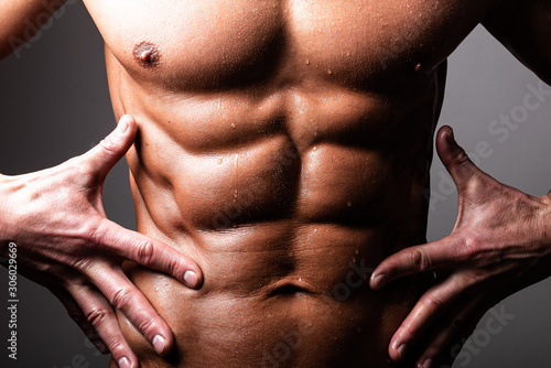 Beautiful, athletic, male torso. In contrast lighting. A man holds his hands near the press.