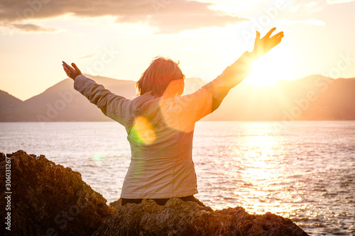 Woman sitting by ocean rejoicing with arms open wide to the sunset photo