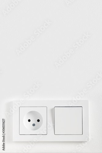 European electric light switch and socket on the painted white wall. Concept of home interior with electric devices. Layout with copy space for your text.