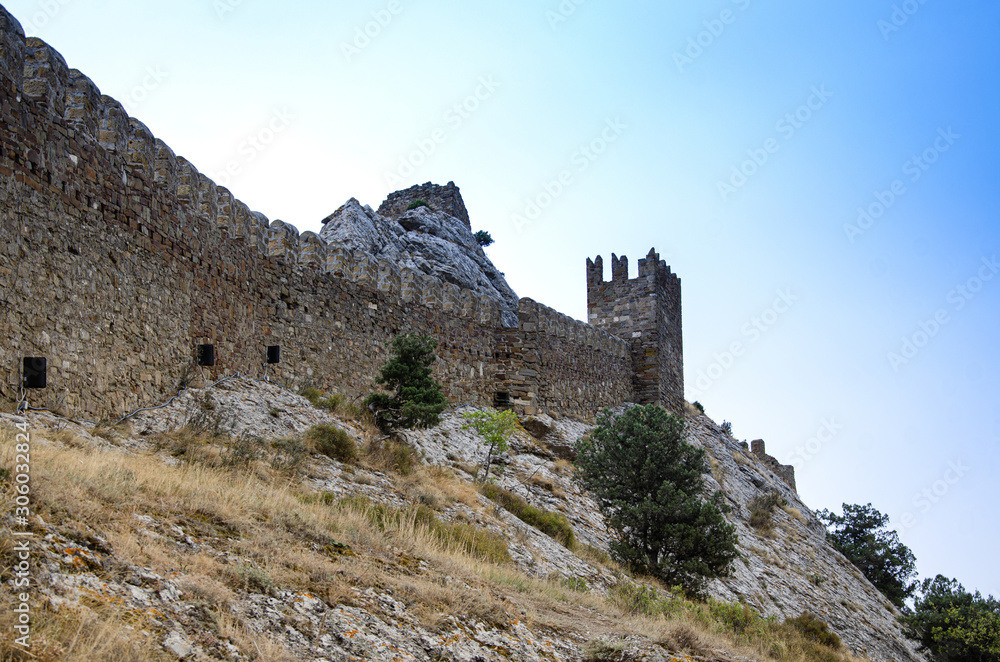 The wall of the old fortress on a high, steep mountain, a slope. Mountain vegetation.