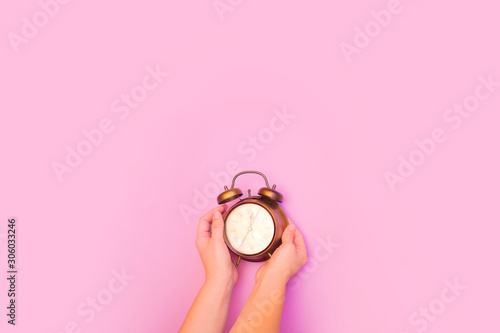 Fototapeta Naklejka Na Ścianę i Meble -  Creative flat lay top view concept of a female hand holding a vintage alarm clock on pink colored paper background with copy space in minimal style, template for text