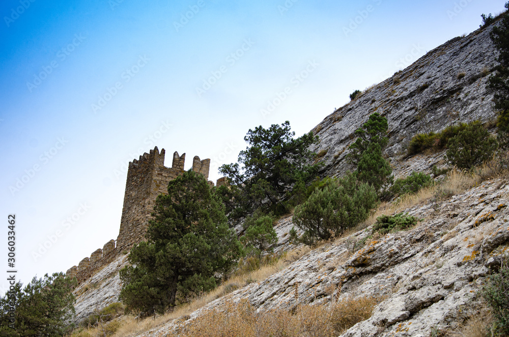 The wall of the old fortress on a high, steep mountain, a slope. Mountain vegetation.