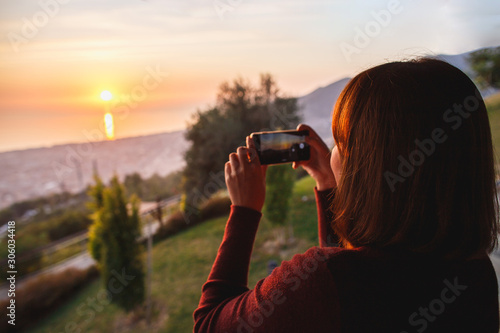 Traveler woman use mobile phone take a photo of beautiful of sunset nature at top of mountain sea view. Deep red sun rays.