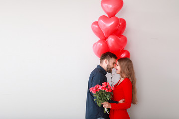 Happy young couple with heart-shaped balloons and flowers on light background. Valentine's Day celebration