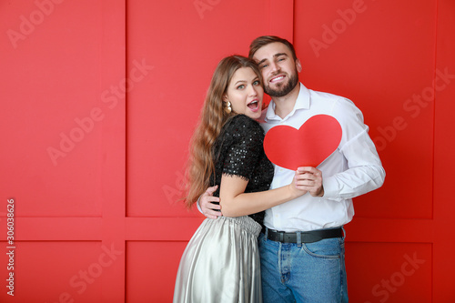 Happy young couple with red heart on color background. Valentine's Day celebration