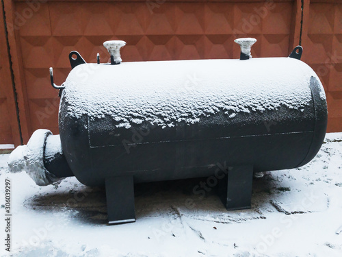 Black Industrial capacitive heater at winter under snow near brown concrete fence. Heat exchanger. photo