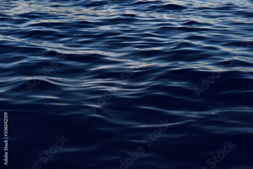 Background of dark blue gentle waves on the sea, on which the sun reflects gently