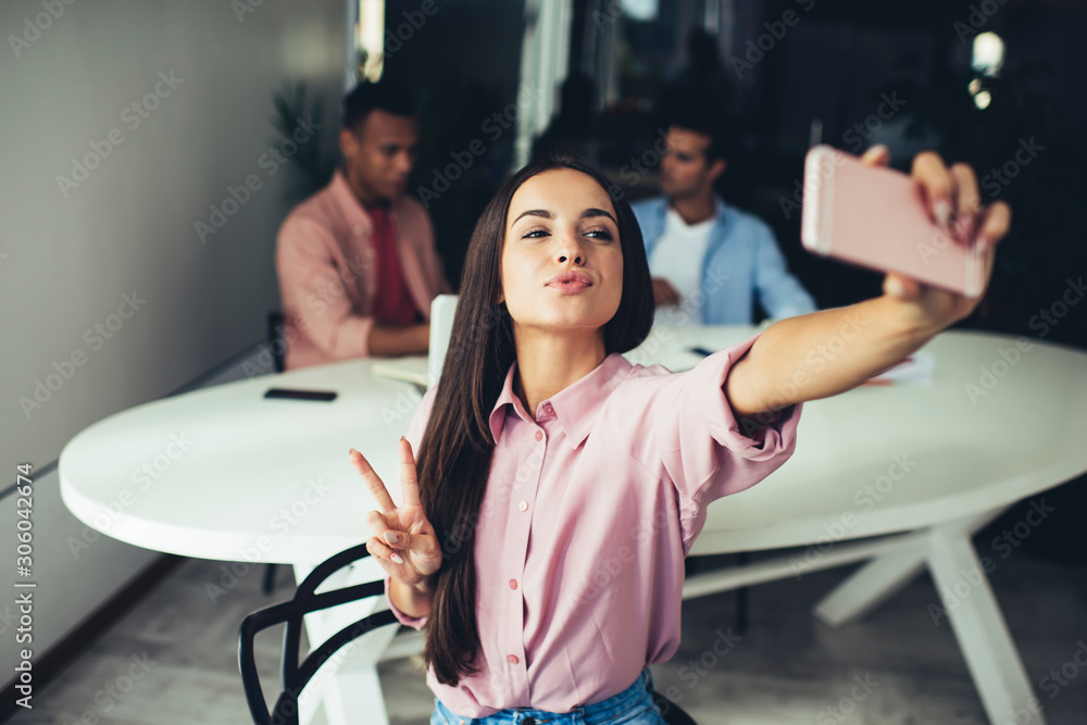 Positive female showing v-sign for taking funny pictures using application for blogging on smartphone gadget, Caucasian hipster girl with duck face clicking selfie photos via modern mobile phone Positive female showing v-sign for taking funny pictures using application for blogging on smartphone gadget, Caucasian hipster girl with duck face clicking selfie photos via modern mobile phone