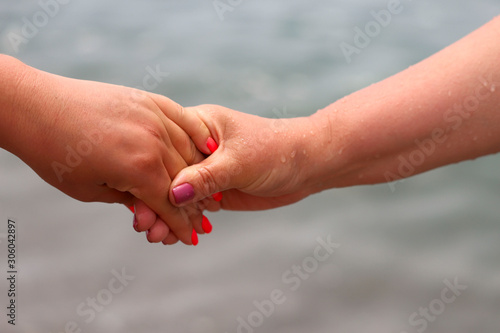 Covered female hands with manicure on a background of the sea. Horizontal, cropped shot, close-up. The concept of friendship and same-sex love.