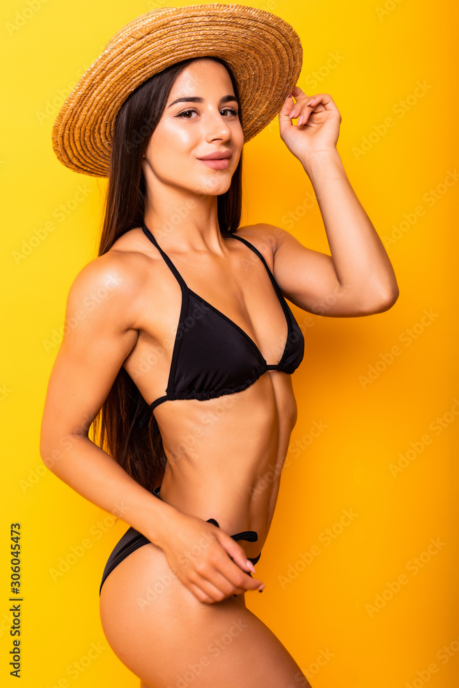 Smiling young woman posing with her black bikini swimsuit on yellow background Smiling young woman posing with her black bikini swimsuit on yellow background