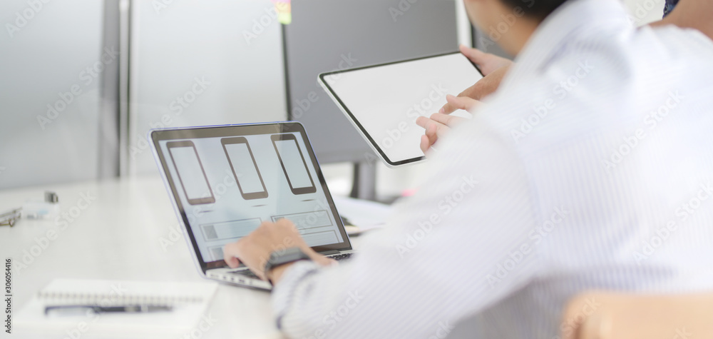 Close-up view of young professional UI web developer working on smartphone application with laptop