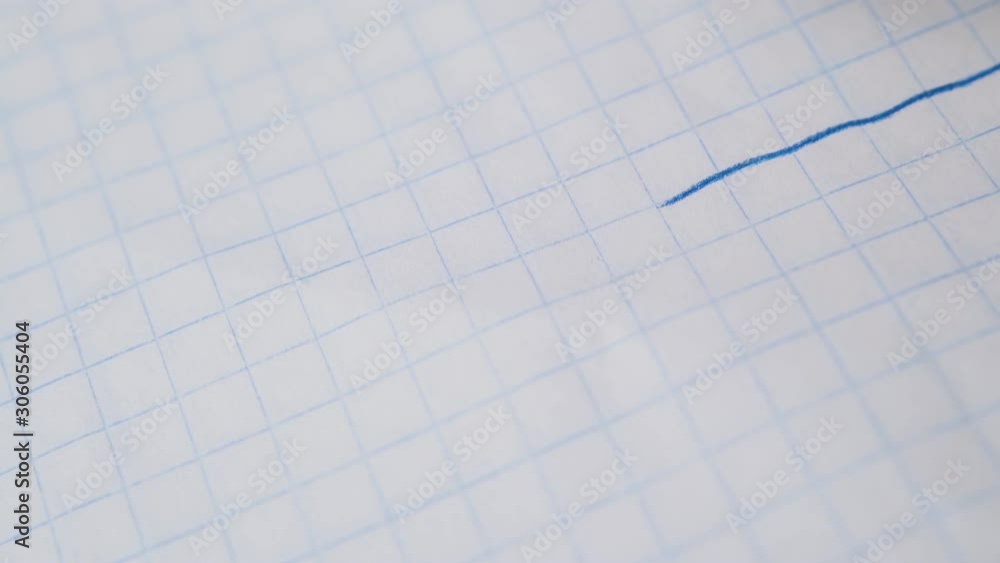 young person draws straight line with blue pencil on checkered paper sheet extreme close view young person draws straight line with blue pencil on checkered paper sheet extreme close view