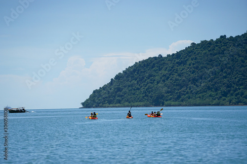 Selective focus on group of travelers canoeing on the surface of sea for touring with seascape and island inbackground