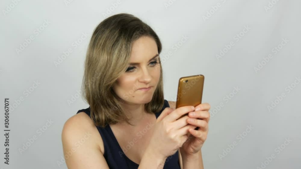Portrait of a beautiful young woman who is posing making a selfie and communicating and looking into a smartphone that is holding in her hands on a white background in the studio. Portrait of a beautiful young woman who is posing making a selfie and communicating and looking into a smartphone that is holding in her hands on a white background in the studio.