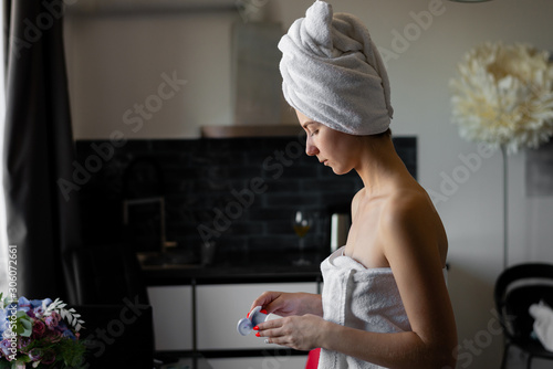 Portrait of a girl in a bath towel applies moisturizer to her body.