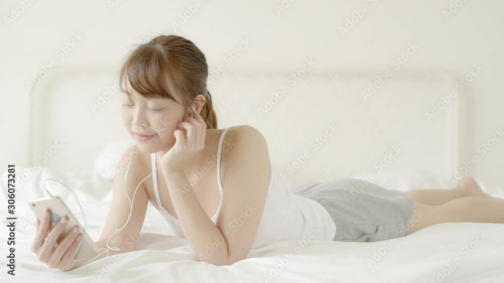 Beautiful portrait young asian woman lying happy earphone listening music with relax and enjoy in the bedroom, girl fun headphone with playing song smart mobile phone, lifestyle concept, slow motion. Beautiful portrait young asian woman lying happy earphone listening music with relax and enjoy in the bedroom, girl fun headphone with playing song smart mobile phone, lifestyle concept, slow motion.