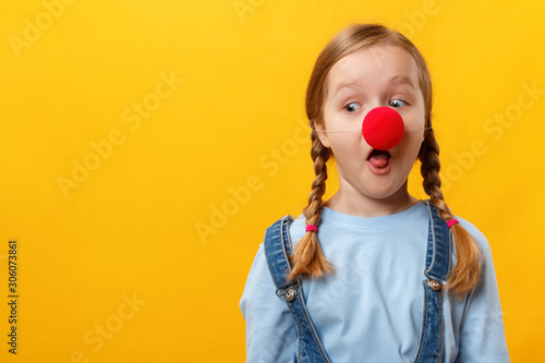 Funny child clown with a red nose. Cheerful little girl on a yellow background. April 1st Fool's Day. Copy space photo