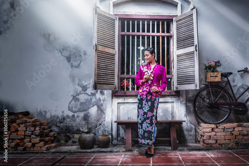 Obraz na płótnie Beautiful Asian woman wearing Nyonya dress her hand holding plastic flower with