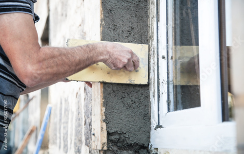 Plasterer using trowel to plastering wall near window.