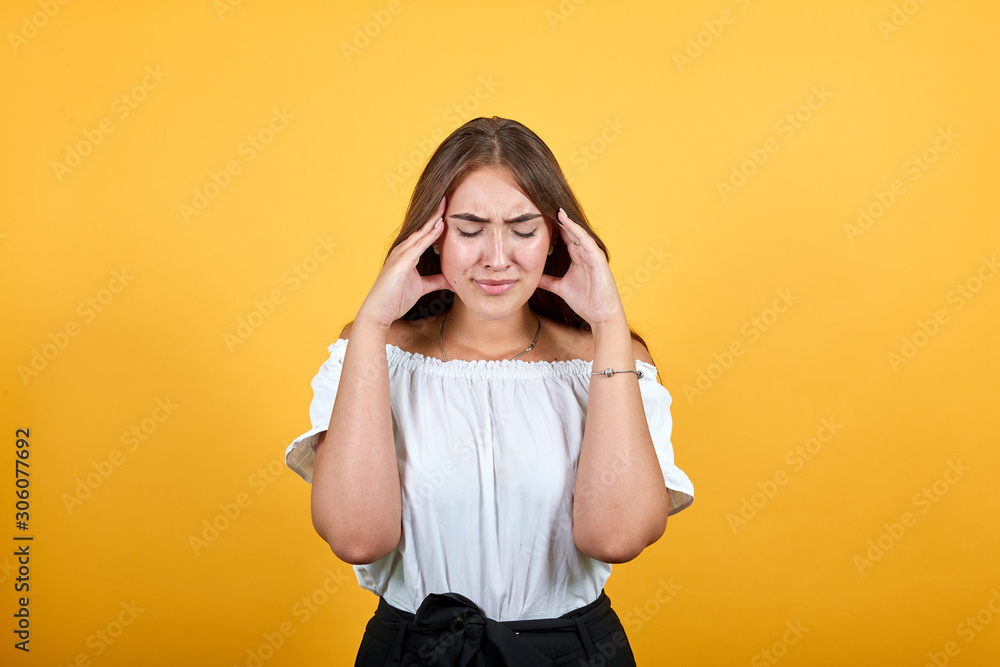 Caucasian young woman keeping hand on head, hrdache, sick isolated on orange background in studio in casual white shirt. People sincere emotions, lifestyle concept. Caucasian young woman keeping hand on head, hrdache, sick isolated on orange background in studio in casual white shirt. People sincere emotions, lifestyle concept.