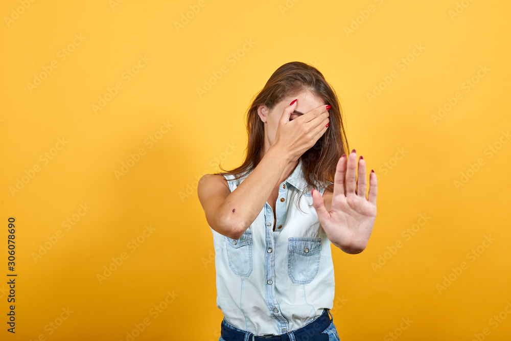Charming caucasian young woman in blue denim shirt covered eyes with hand, doing stop gesture isolated on orange background in studio. People sincere emotions, lifestyle concept. Charming caucasian young woman in blue denim shirt covered eyes with hand, doing stop gesture isolated on orange background in studio. People sincere emotions, lifestyle concept.