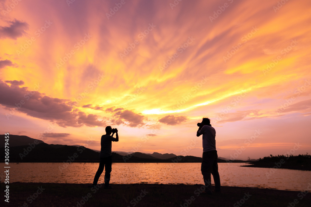 Silhouette of man taking pictures with his camera while sunset hour; against twilight sky over a mountain. Traveling and vacation concept.