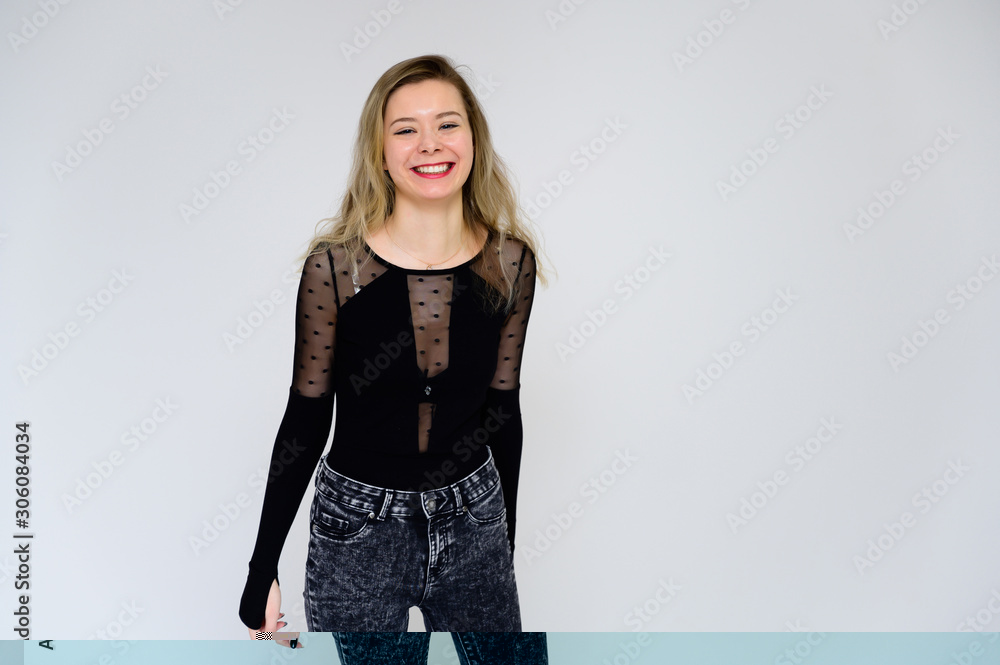 Concept of a woman talking to the camera. A photo of a pretty smiling girl with long beautiful curly hair in a black T-shirt on a white background is standing right in front of the camera. Concept of a woman talking to the camera. A photo of a pretty smiling girl with long beautiful curly hair in a black T-shirt on a white background is standing right in front of the camera.